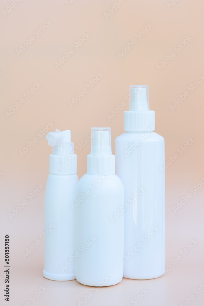 Set of three white spray bottles on beige background. Copy space, vetrical format Set of three white spray bottles on beige background. Copy space, vetrical format
