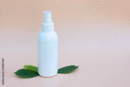 White spray bottle with medical and spa treatment for caring hair  hands anf face  body. Organic spa treatment  eco cosmetic products concept. Beige background with leaves and copy space.