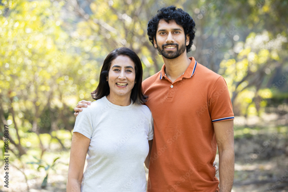 Fototapeta premium Portrait of happy indian couple standing outdoors in the park, Smiling urban city man and woman wearing casual t-shirt, looking at camera. husband wife.