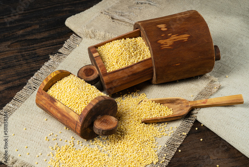 Raw organic millet grits in a wooden box with a spoon on a coarse napkin.