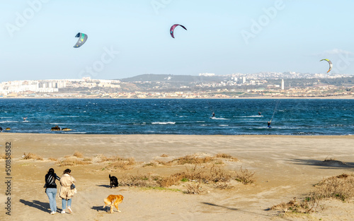 Kitesurf school, Marina Sidi Fredj sailing club, Staoueli. Beach surfers. Girls walking in the sand with dogs. Deep blue sea waves and City coast. photo