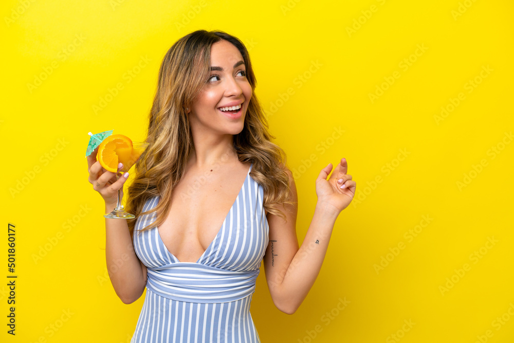 Young caucasian woman isolated on yellow background in swimsuit and holding a cocktail Young caucasian woman isolated on yellow background in swimsuit and holding a cocktail