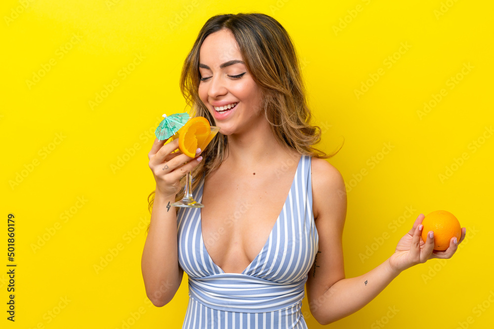 Young caucasian woman isolated on yellow background in swimsuit and holding a cocktail Young caucasian woman isolated on yellow background in swimsuit and holding a cocktail