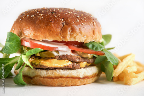 Close up of burger with beef patty, tomato, lettuce, cheese and fries at white background. American fast food for lunch or dinner. Delicious to go food. Front view.