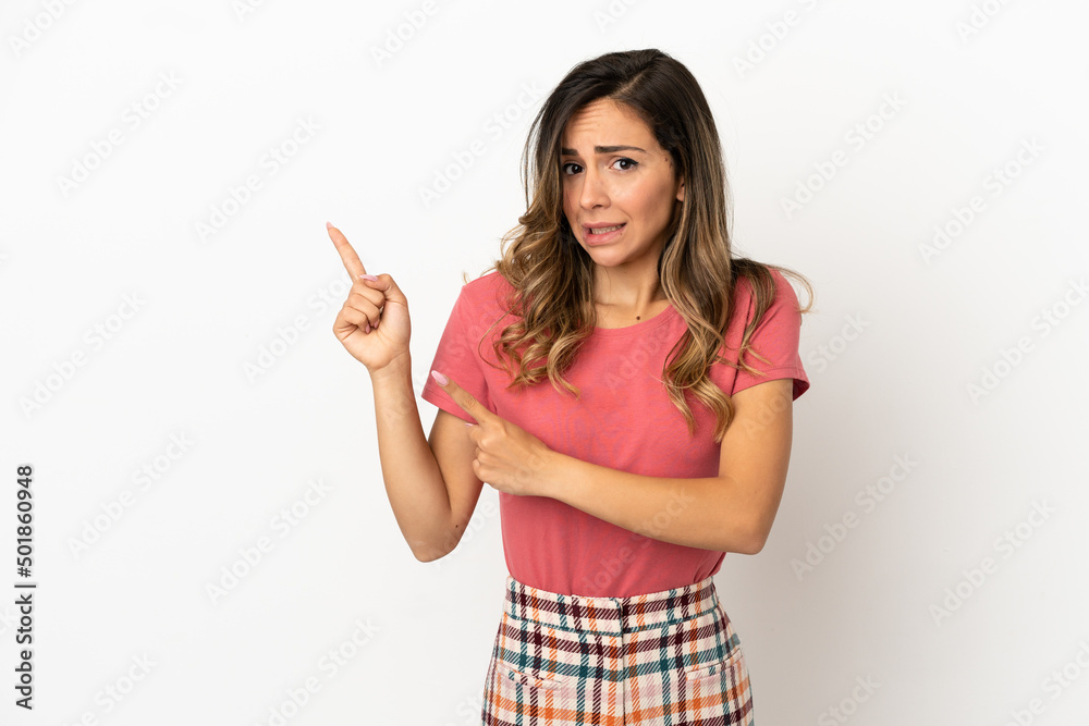 Young woman over isolated background frightened and pointing to the side Young woman over isolated background frightened and pointing to the side