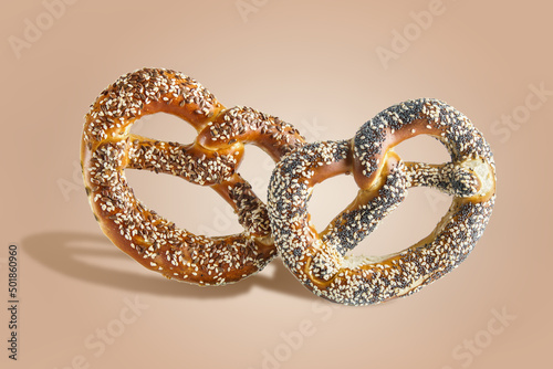 Two Bavarian pretzels with sesame and poppy seeds at pale brown background. Delicious traditional German buns. Bakery items flying. Levitation concept. Front view.