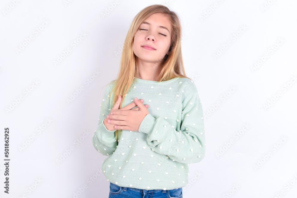 little caucasian kid girl wearing fashion sweater over blue background smiling with hands on chest with closed eyes and grateful gesture on face. Health concept. little caucasian kid girl wearing fashion sweater over blue background smiling with hands on chest with closed eyes and grateful gesture on face. Health concept.