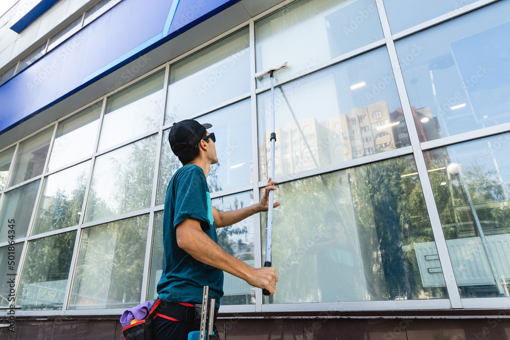 Male professional cleaning service worker in overalls cleans the windows and shop windows of a store with special equipment Male professional cleaning service worker in overalls cleans the windows and shop windows of a store with special equipment