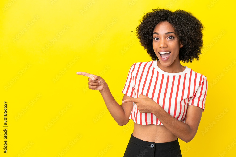 Young African American woman isolated on yellow background surprised and pointing side Young African American woman isolated on yellow background surprised and pointing side