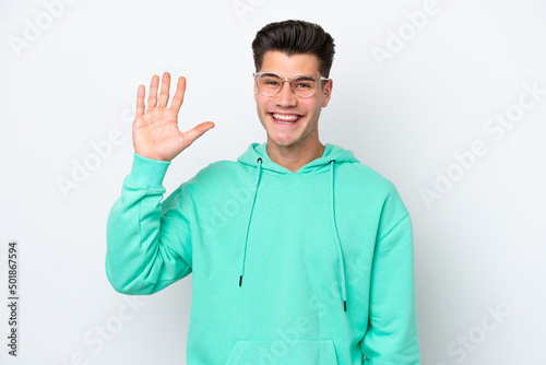 Young handsome caucasian man isolated on white bakcground saluting with hand with happy expression