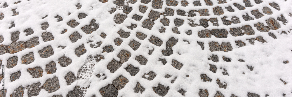 Fototapeta premium Old cobblestone pavement with snow in winter. Panoramic image