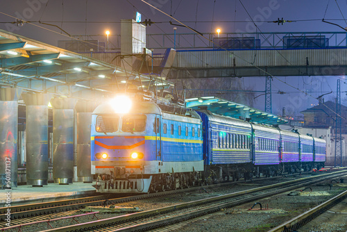 Local passenger train departs from the platform of the evening railway station.