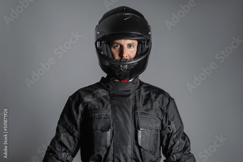 Studio shot of Motorcyclist biker in black equipment looking at camera.
