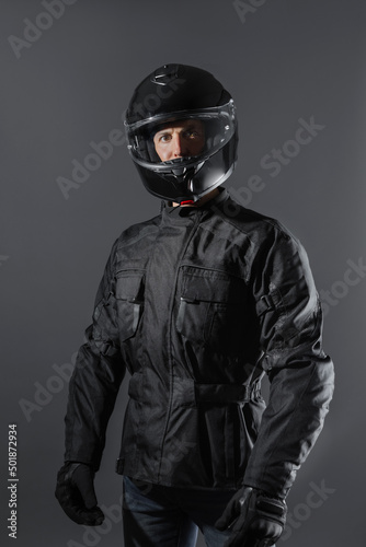 Studio shot of Motorcyclist biker in black equipment looking at camera.