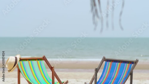 Colorful beach chairs with hat on the beach and sea waves and blue sky in the background.