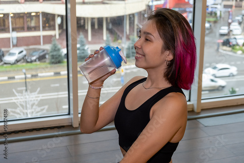 Young athletic woman drinking water from a flask after doing fitness,