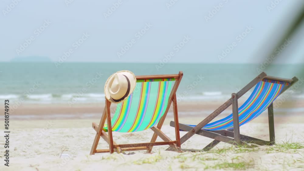 Colorful beach chairs with hat on the beach and sea waves and blue sky in the background.