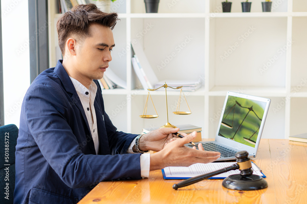 Young Asian lawyer working with papers and laptop, golden hammer and scales, legal counsel's concept of injustice in the office. Young Asian lawyer working with papers and laptop, golden hammer and scales, legal counsel's concept of injustice in the office.