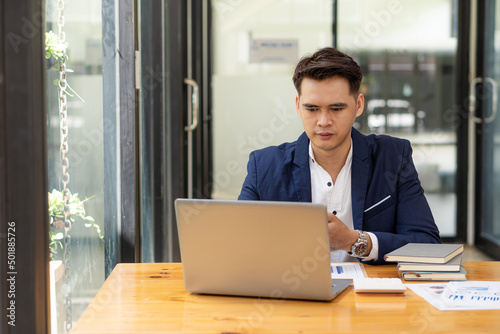 Asian male businessman with documents and laptop computer doing accounting and analytics work. data charts and graphs and use a calculator to calculate numbers Business Finance and Accounting Concepts