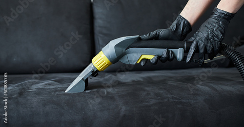 Cleaning service company employee removing dirt from furniture in flat with professional equipment. Female housekeeper arm cleaning sofa with washing vacuum cleaner close up