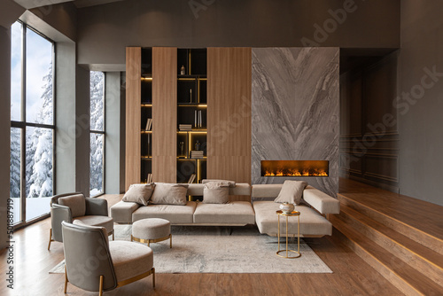 living room, marble wall fireplace and stylish bookcase in chic expensive interior of luxury country house with a modern design with wood and led light, gray furniture with gold elements