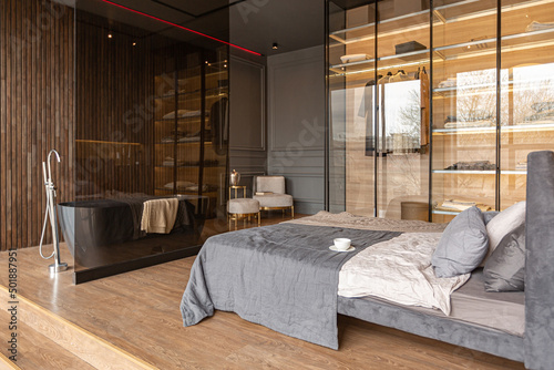 bedroom and freestanding bath behind a glass partition in a chic expensive interior of a luxury home with a dark modern design with wood trim and led light