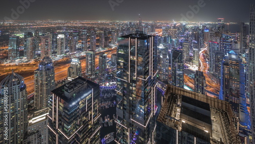 Panorama showing Dubai Marina and JLT district with traffic on highway between skyscrapers aerial night timelapse.