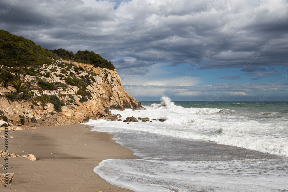Stormy coastline with water splash and dark sky, sandy beach with turquoise sea, Sitges, Spain Stormy coastline with water splash and dark sky, sandy beach with turquoise sea, Sitges, Spain
