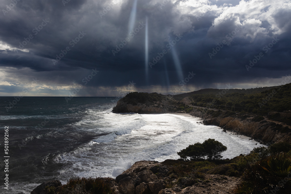 Stormy coastline with water splash and dark sky, sandy beach with turquoise sea, Sitges, Spain