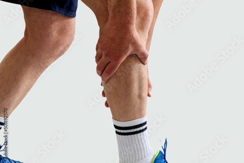 Man in sport clothes holding leg muscle pain and numbness from muscle cramps isolated on white background. Calf muscle pain in runner.  photo