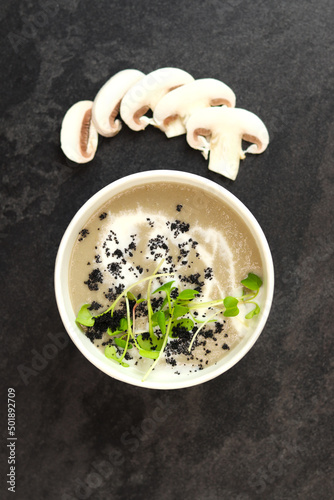 French cuisine hot food delivery - mushrooms soup closeup in eco paper bowl on black background. Delivery healthy eating concept.