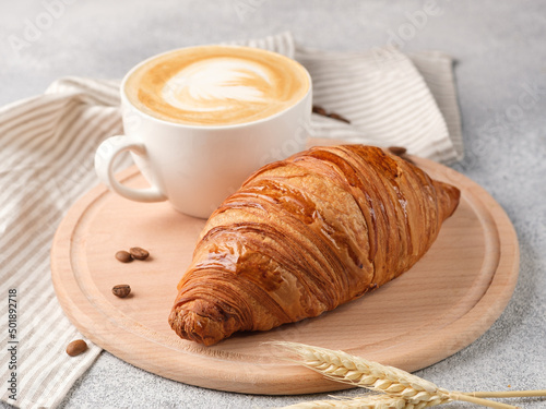 Large croissant and a cup of cappuccino on a light background