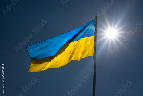 Ukrainian flag against a blue sky with a bright sun.