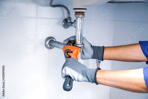 Leinwand Poster Technician plumber using a wrench to repair a water pipe under the sink