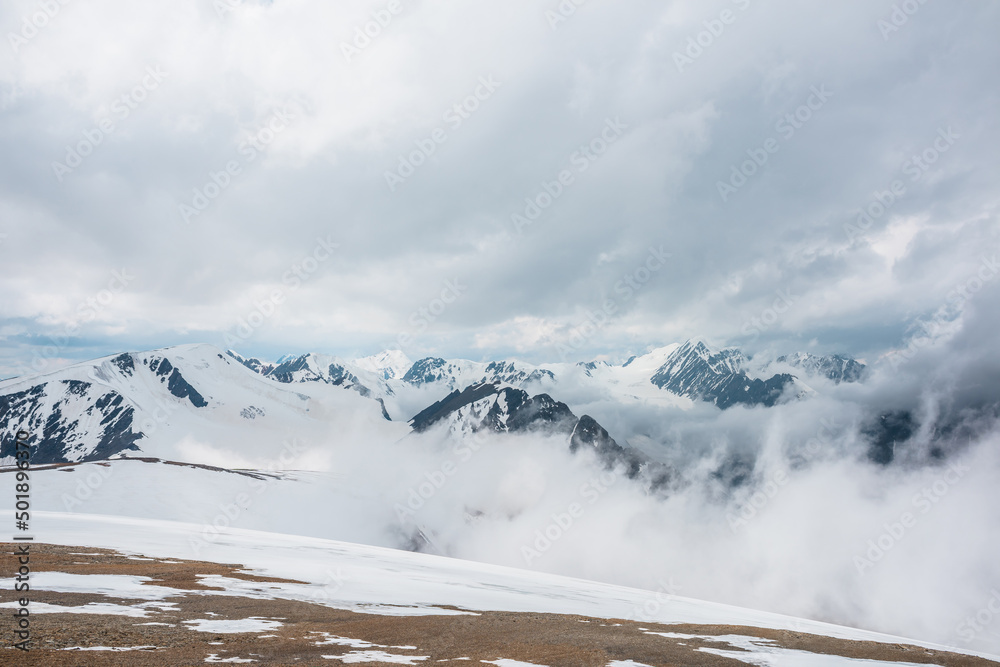 Awesome aerial view to high snowy mountains in dense low clouds. Minimal landscape with beautiful mountain peaks in thick clouds. Simple minimalism with snow mountain tops in cloudy sky above clouds.
