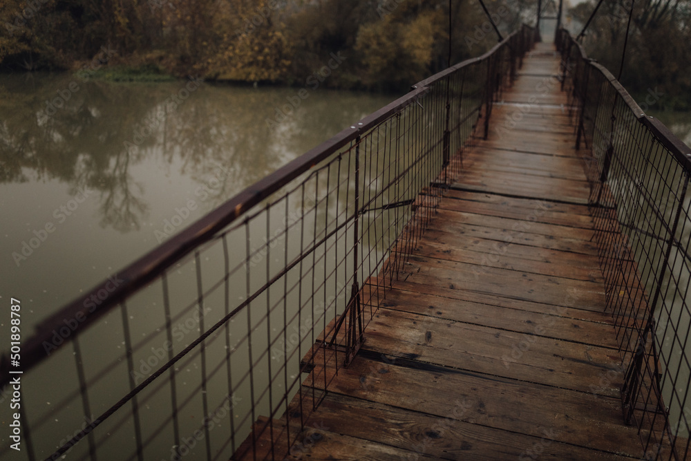 Eerie scenery of a wooden suspension bridge over the river in a cloudy day Eerie scenery of a wooden suspension bridge over the river in a cloudy day
