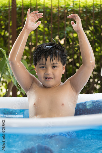Portrait of a boy playing in the inflatable pool at his home. Cool summer activities. © wacharaphong