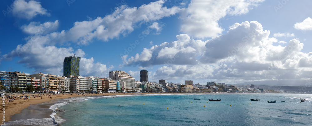 Panoramic view of a sandy beach and tourists under a cloudy sky in Las Palmas de Gran Canaria, Spain
