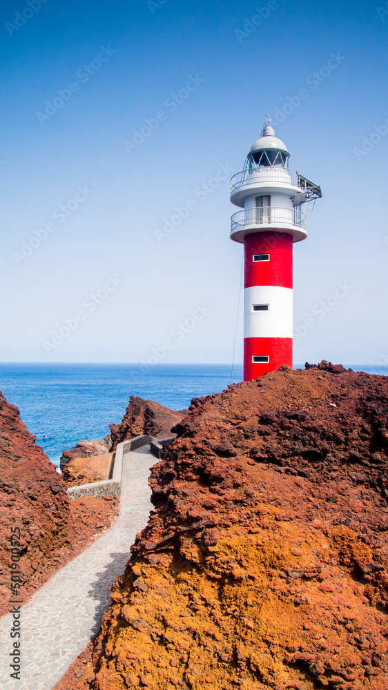 Beautiful red and white lighthouse building on volcanic shore of Tenerife Island in Spain. Atlantic Ocean background, vertical photo.