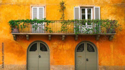 Orange Italian house facade in a typical town of Italy with green doors and balcony with white shutters. Pretty postcard background from Italy.