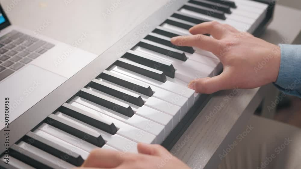 Man with a blue shirt playing keyboard on a gray desk with a computer in front of him Man with a blue shirt playing keyboard on a gray desk with a computer in front of him