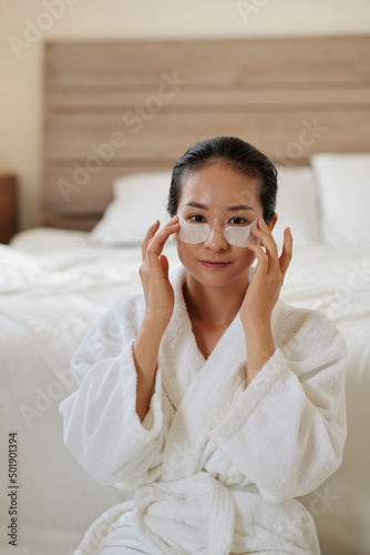 Portrait of young Vietnamese woman applying undereye patches to get rid of morning puffiness and dark circles