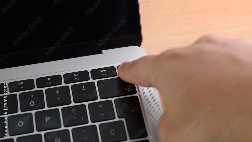 Hand is pressing power on key on laptop computer, close up. Finger