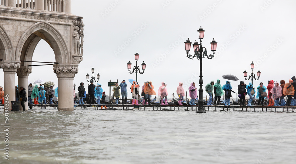 People with rain gear walking on the elevated walkway in the submerged Square of Saint Mark in Venice in Italy at high tide
