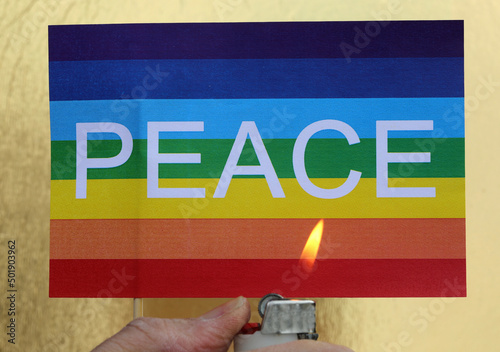 hand with lighter and fire burning multicolored flag with text PEACE