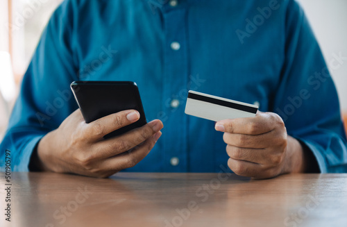 Businessman using smartphone and credit card for online shopping at home with copy space. E-payment technology, shopaholic lifestyle, or mobile phone financial application concept
