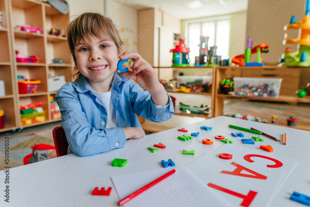Fototapeta premium Little girl writing and playing with letters at kindergarten