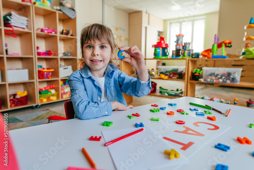 Little girl writing and playing with letters at kindergarten