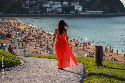 Young brunette girl walking to the beach at summer with long orange dress