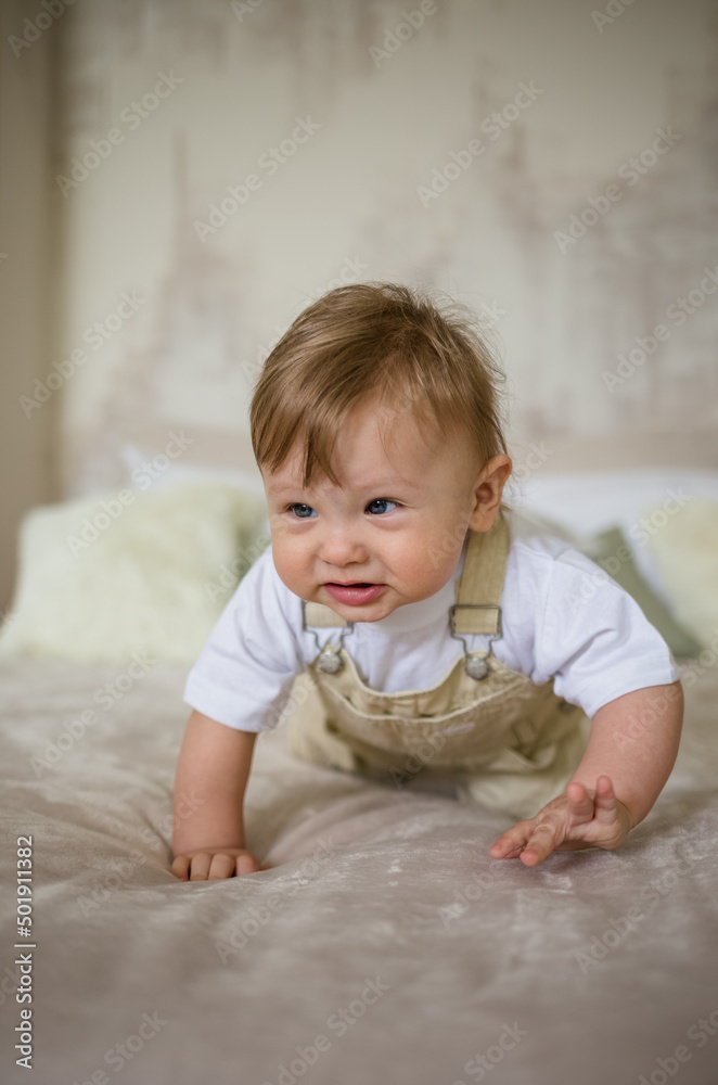 funny little boy crawling on the bed in the bedroom. caucasian little boy with strabismus learning to crawl funny little boy crawling on the bed in the bedroom. caucasian little boy with strabismus learning to crawl